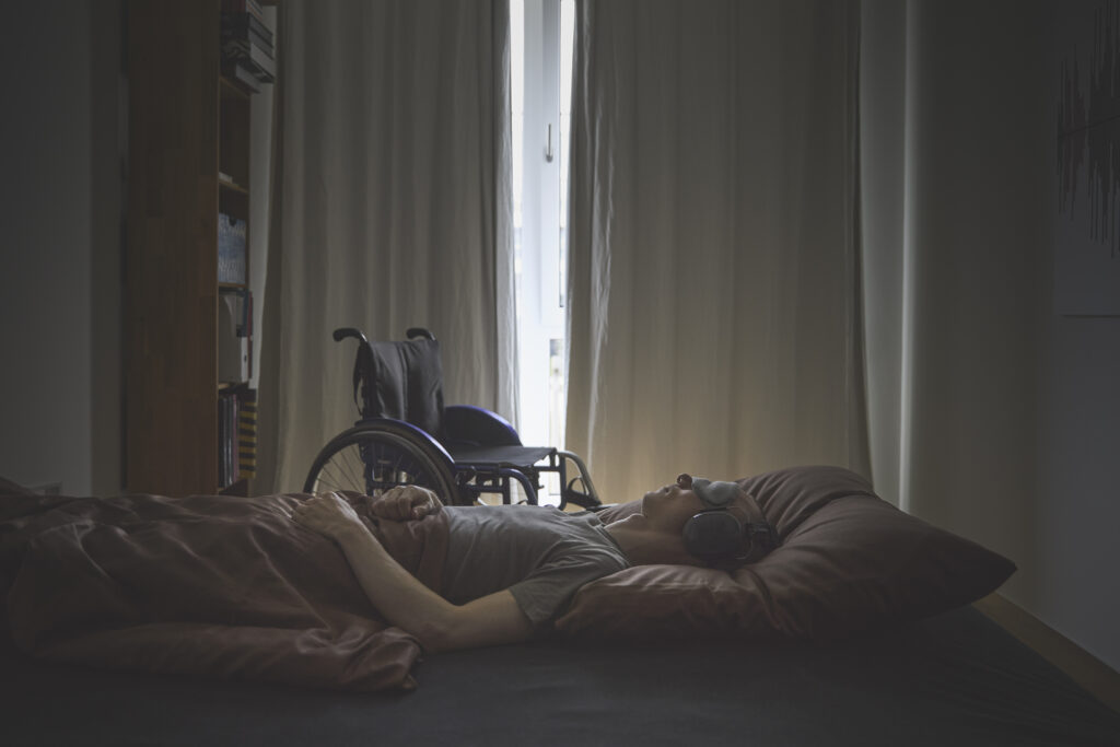 Ein ME/CFS-Schwerstbetroffener liegt mit Kopfhörern und Schlafmaske im abgedunkelten Raum.